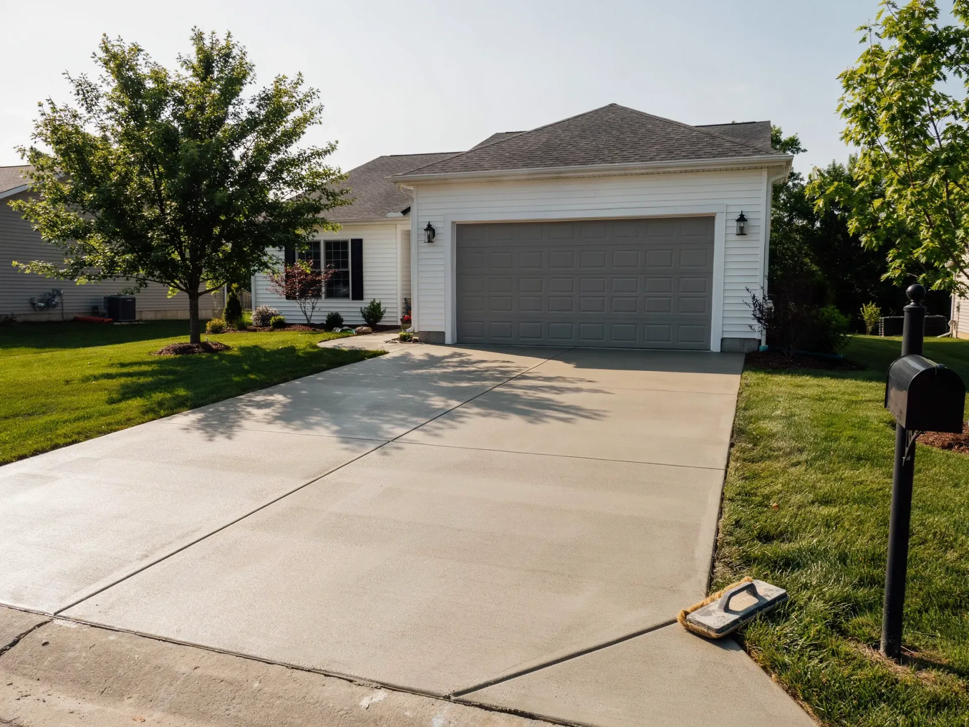 Suburban house with two-car garage, wide concrete driveway, and a tree in the front yard