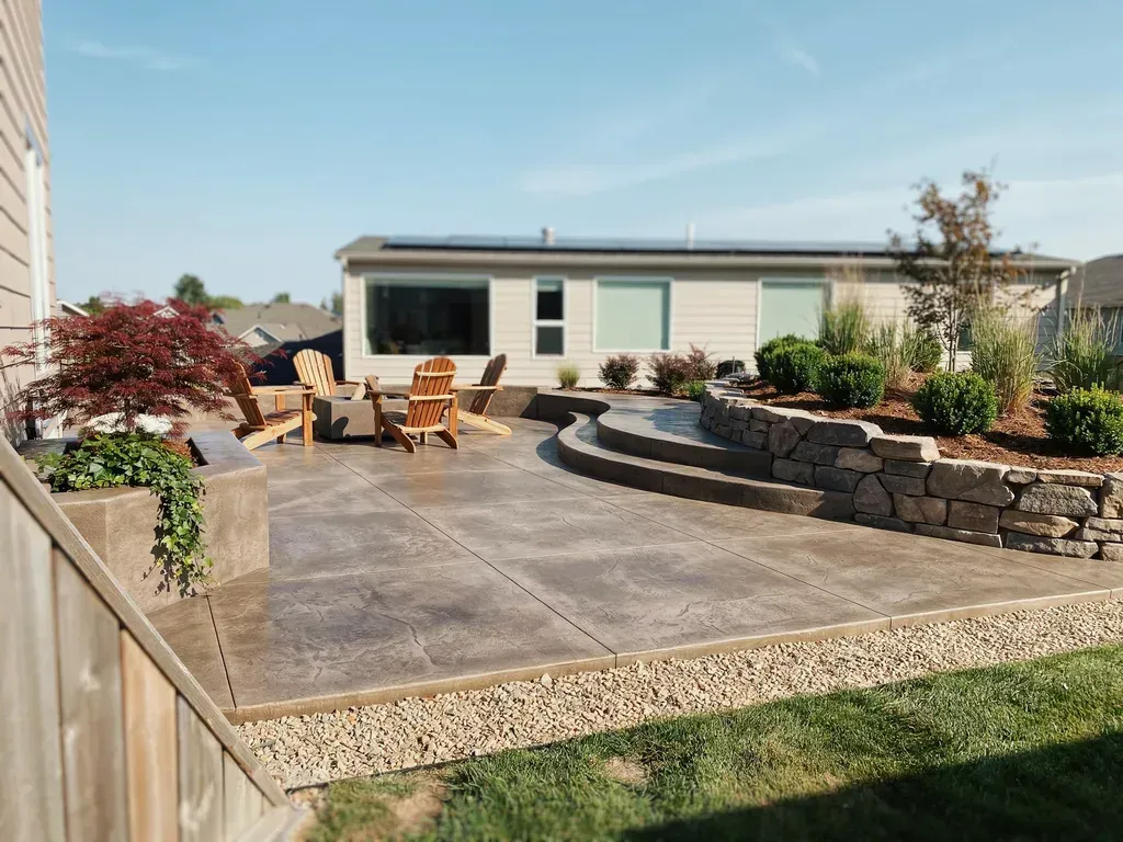 Backyard patio with stone seating wall, outdoor chairs, and a modern house under a clear sky