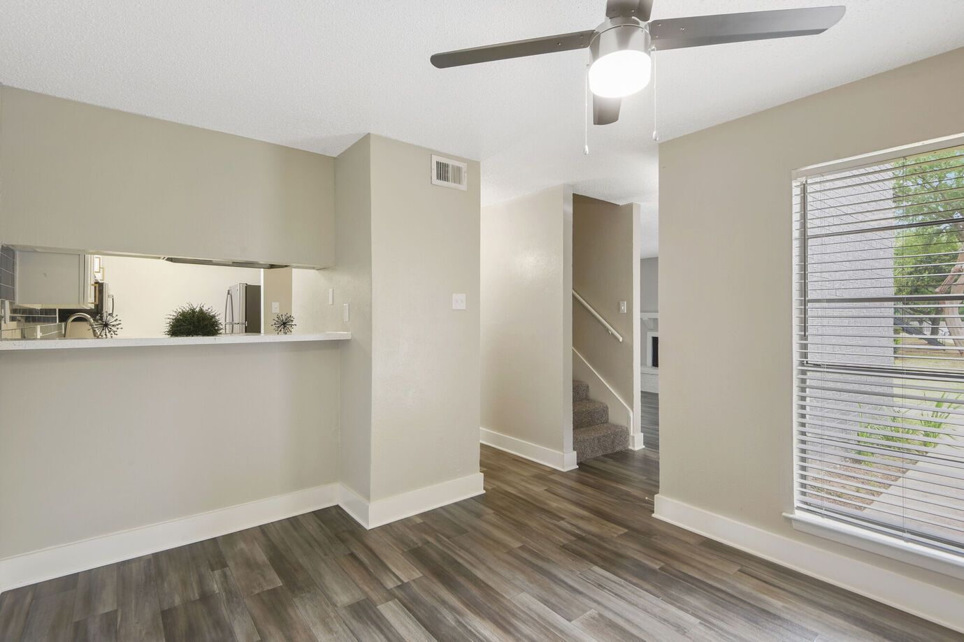 Empty dining room with gray wood-look floor, neutral walls, open kitchen bar, and a window.