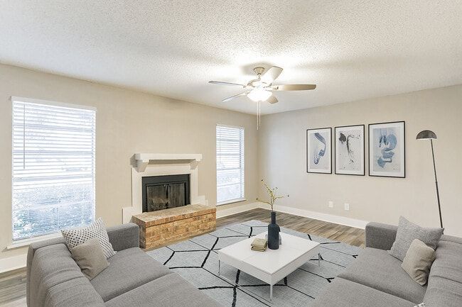 Living room with gray couches, fireplace, and art. Sunlight streams through windows.