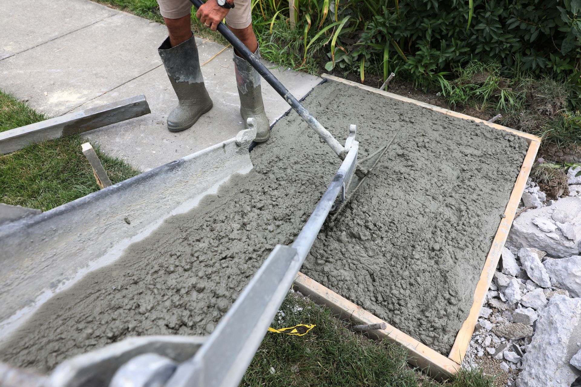 Worker smoothing wet concrete in a wooden form with a long-handled tool outdoors
