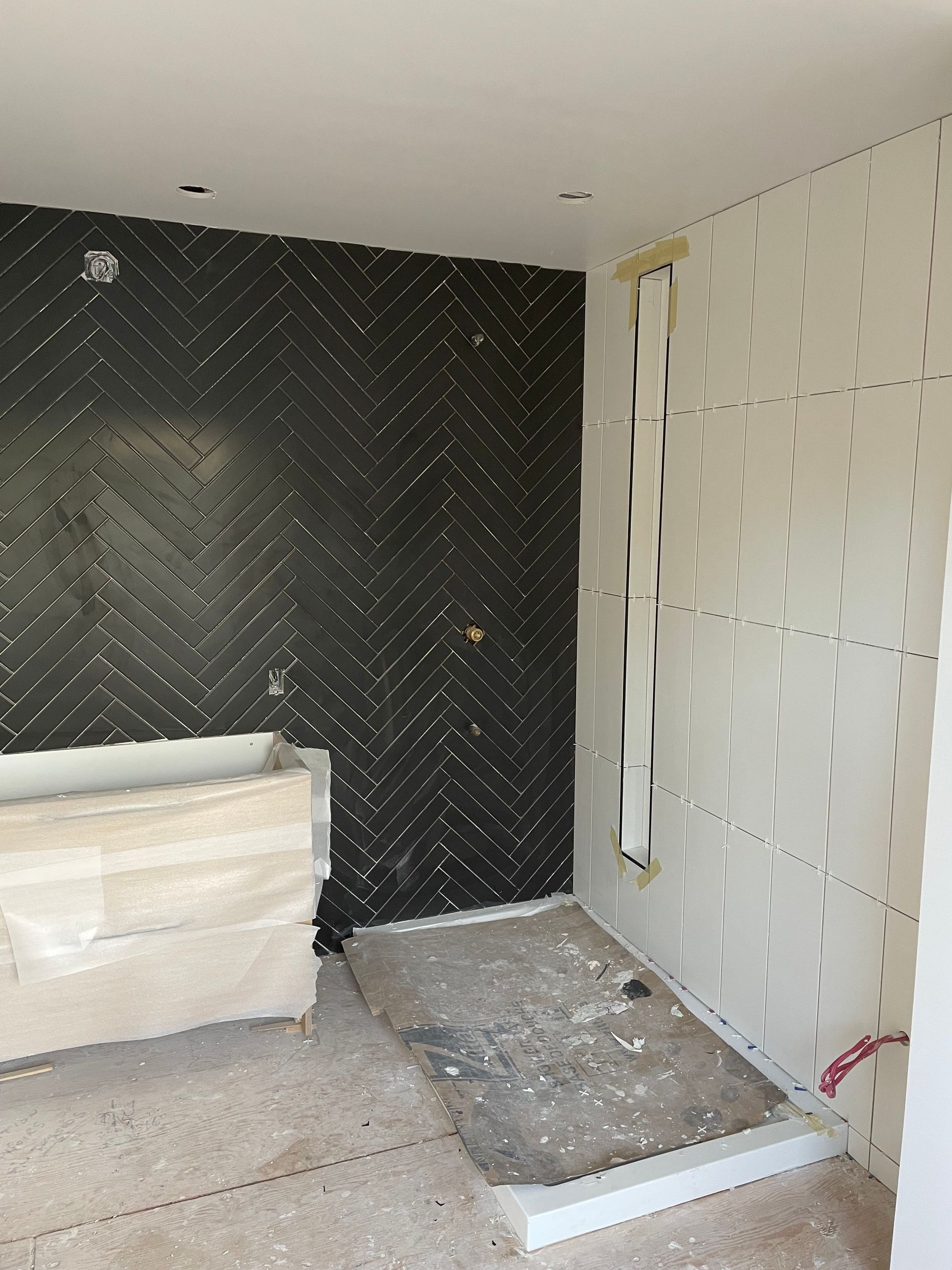 Salle de bains en construction avec mur carrelé de carreaux noirs à chevrons et cloisons sèches blanches.