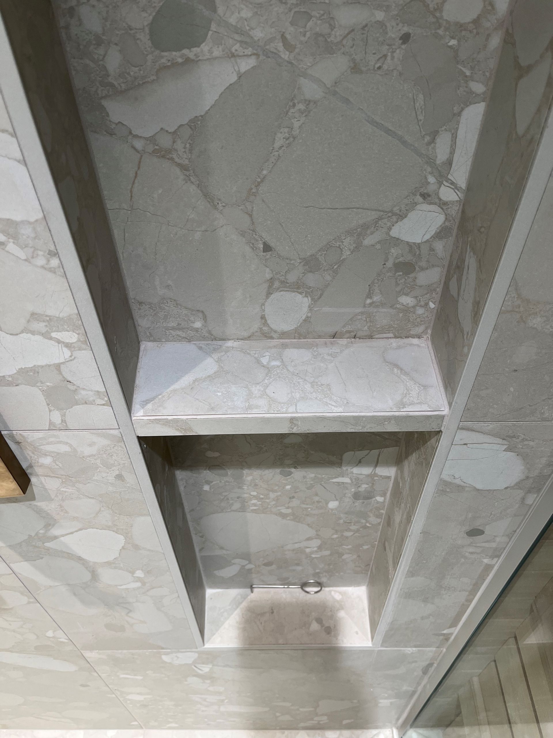 Étagère de douche encastrée dans un mur carrelé de carreaux gris à motifs avec des accents linéaires.