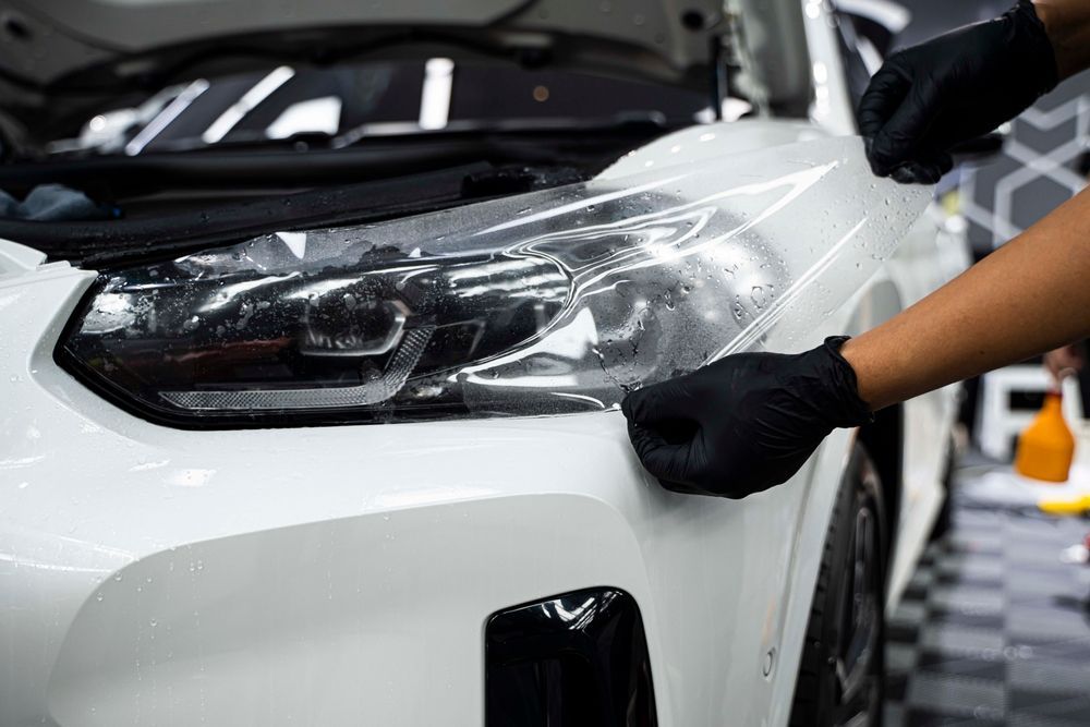 A person is applying a protective film to the headlight of a car.