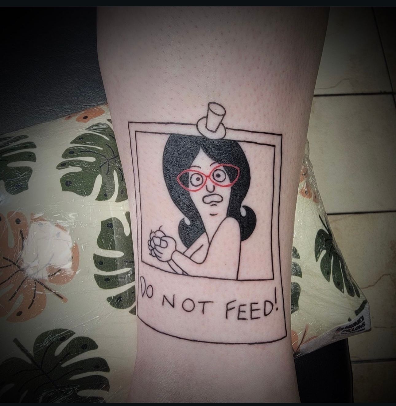 A tattoo of a woman with glasses and a top hat says do not feed