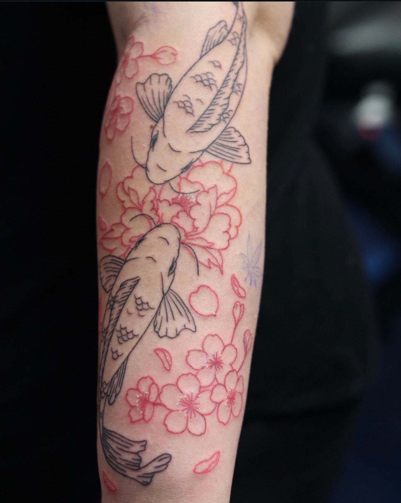 A tattoo of two fish and flowers on a person 's arm