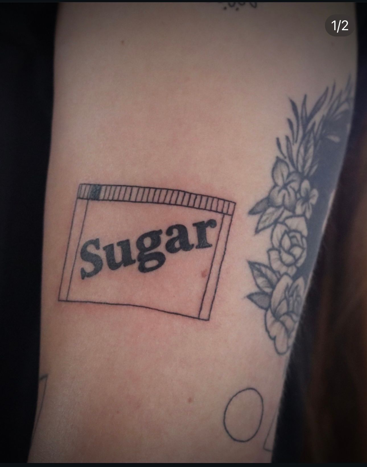A person has a tattoo of a bag of sugar on their arm