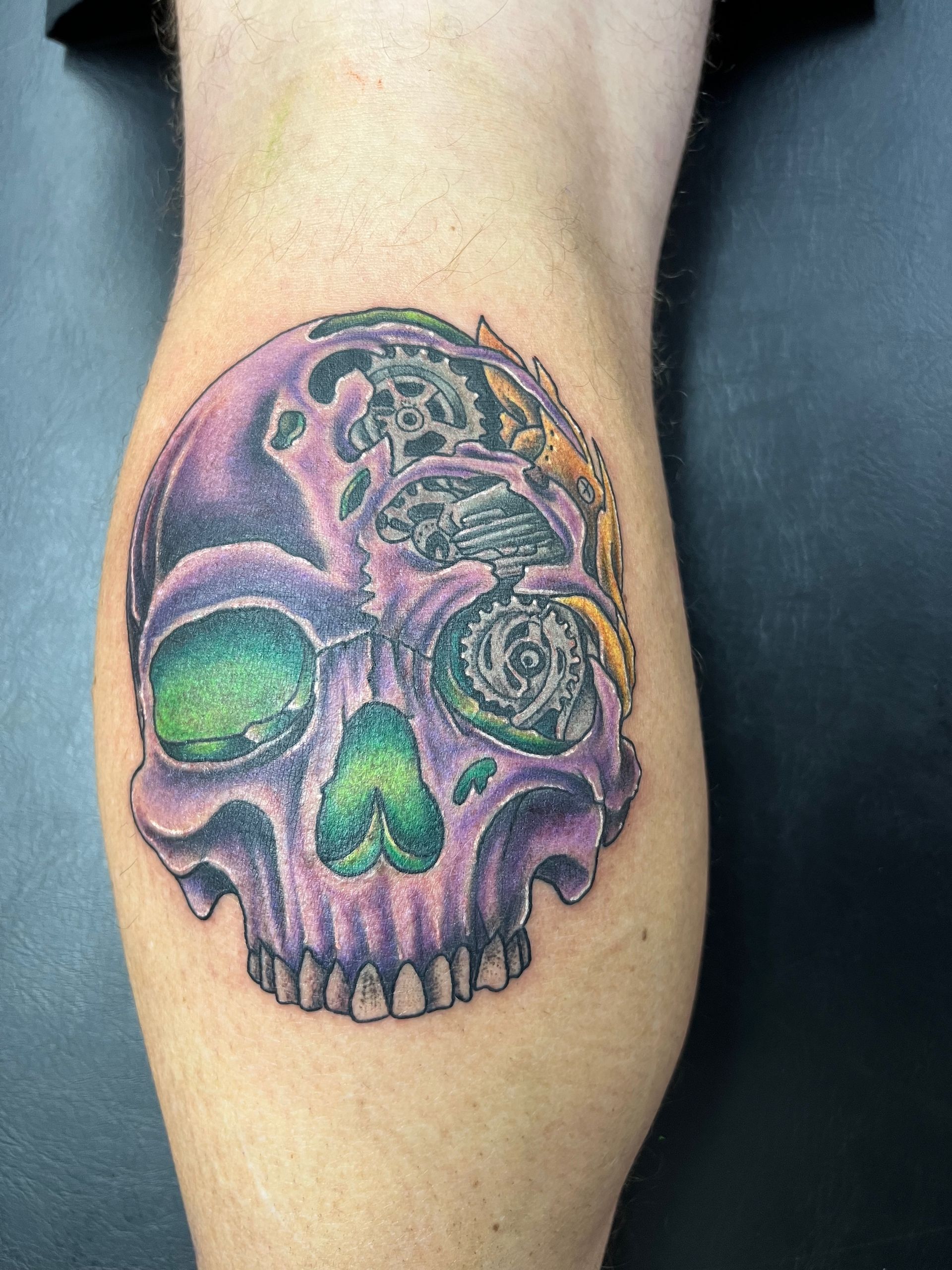 A purple and green skull tattoo on a person 's leg