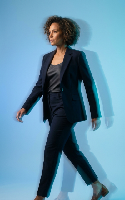 Person in a navy suit walking against a light blue background.