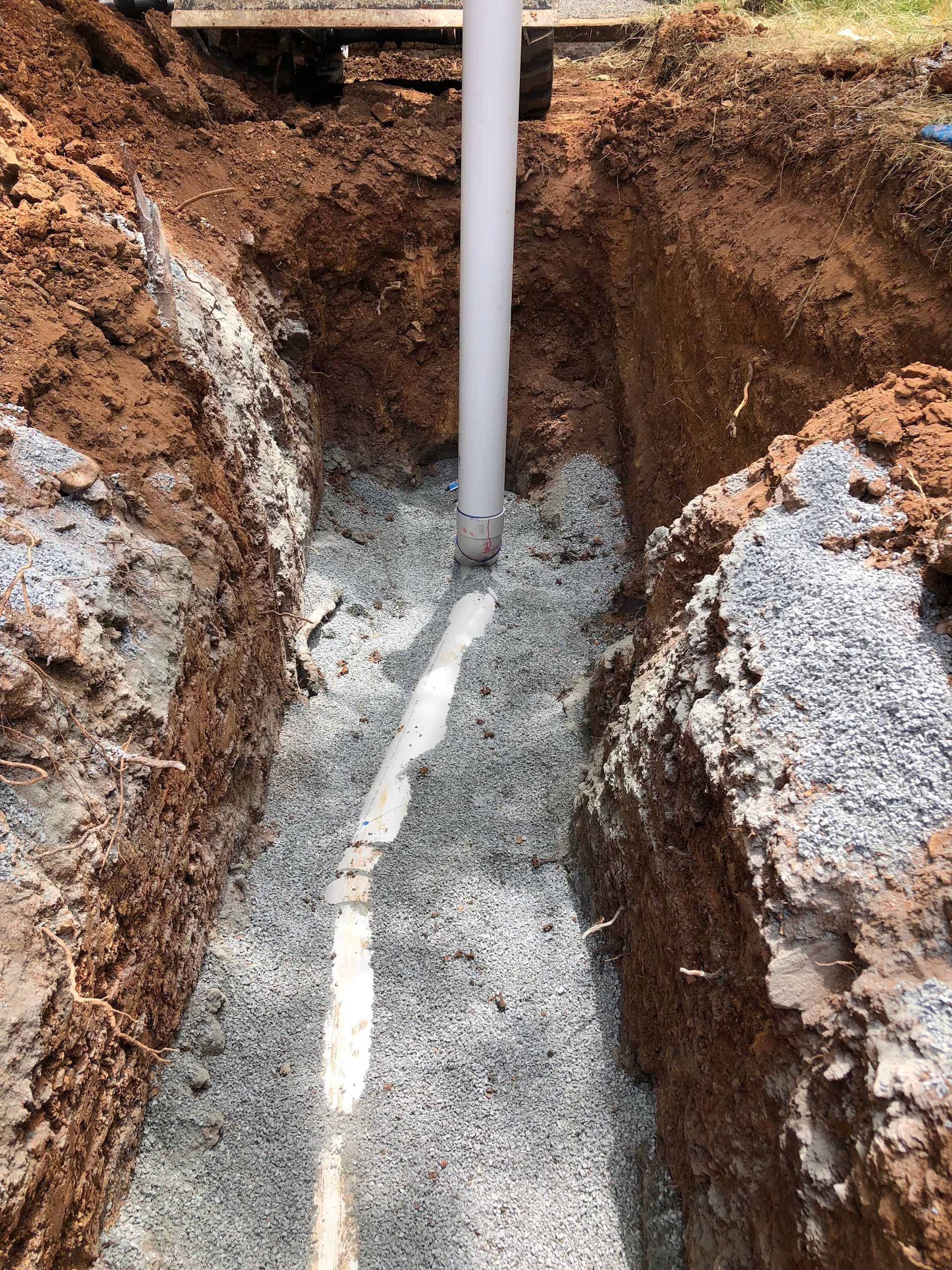 Trench with gravel and concrete around a vertical white pipe in the ground — Plumbing in Canberra, ACT