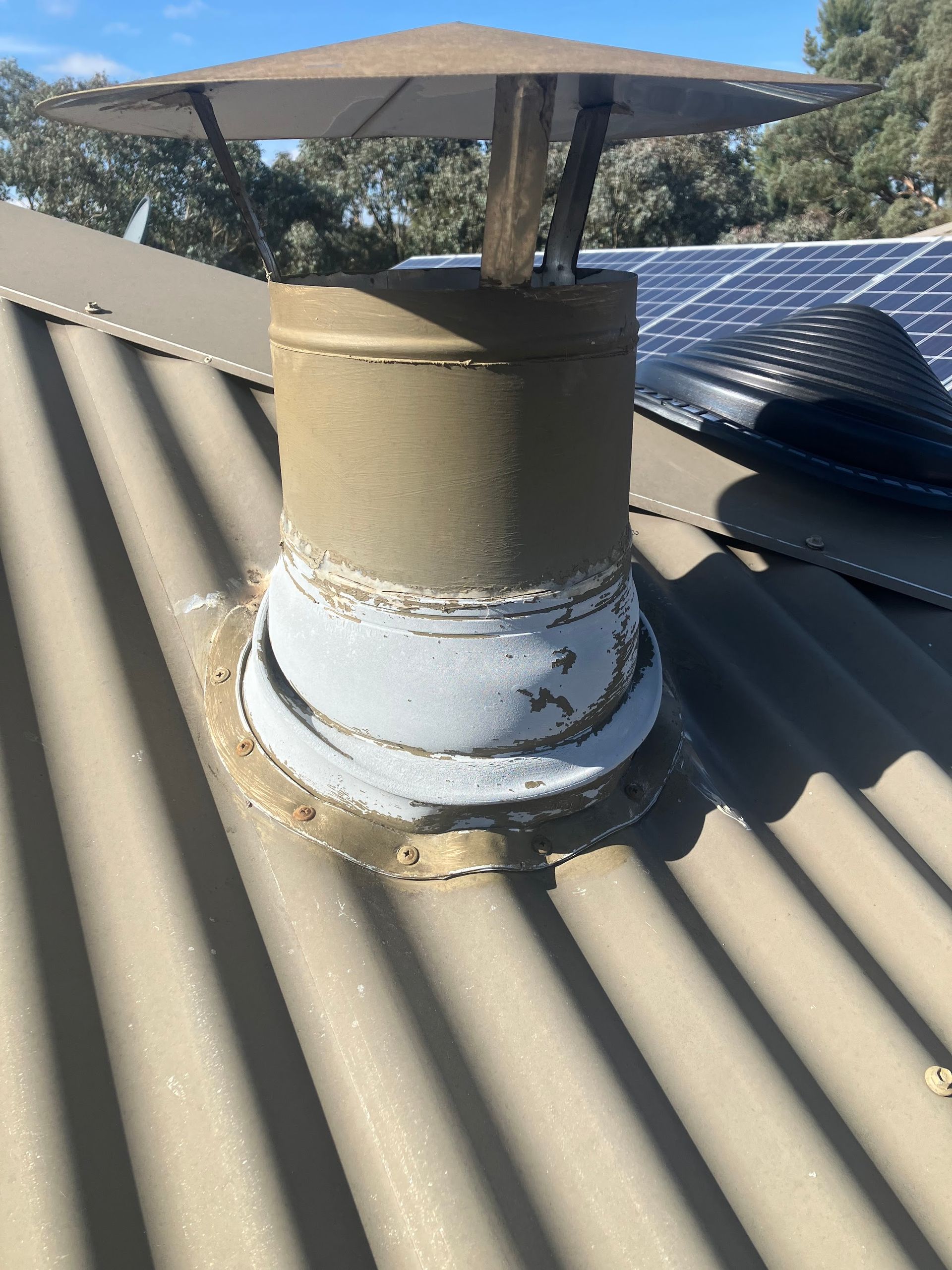 Rooftop vent pipe with a metal cap on a corrugated metal roof, showing rust and peeling paint — Plumbing in Canberra, ACT