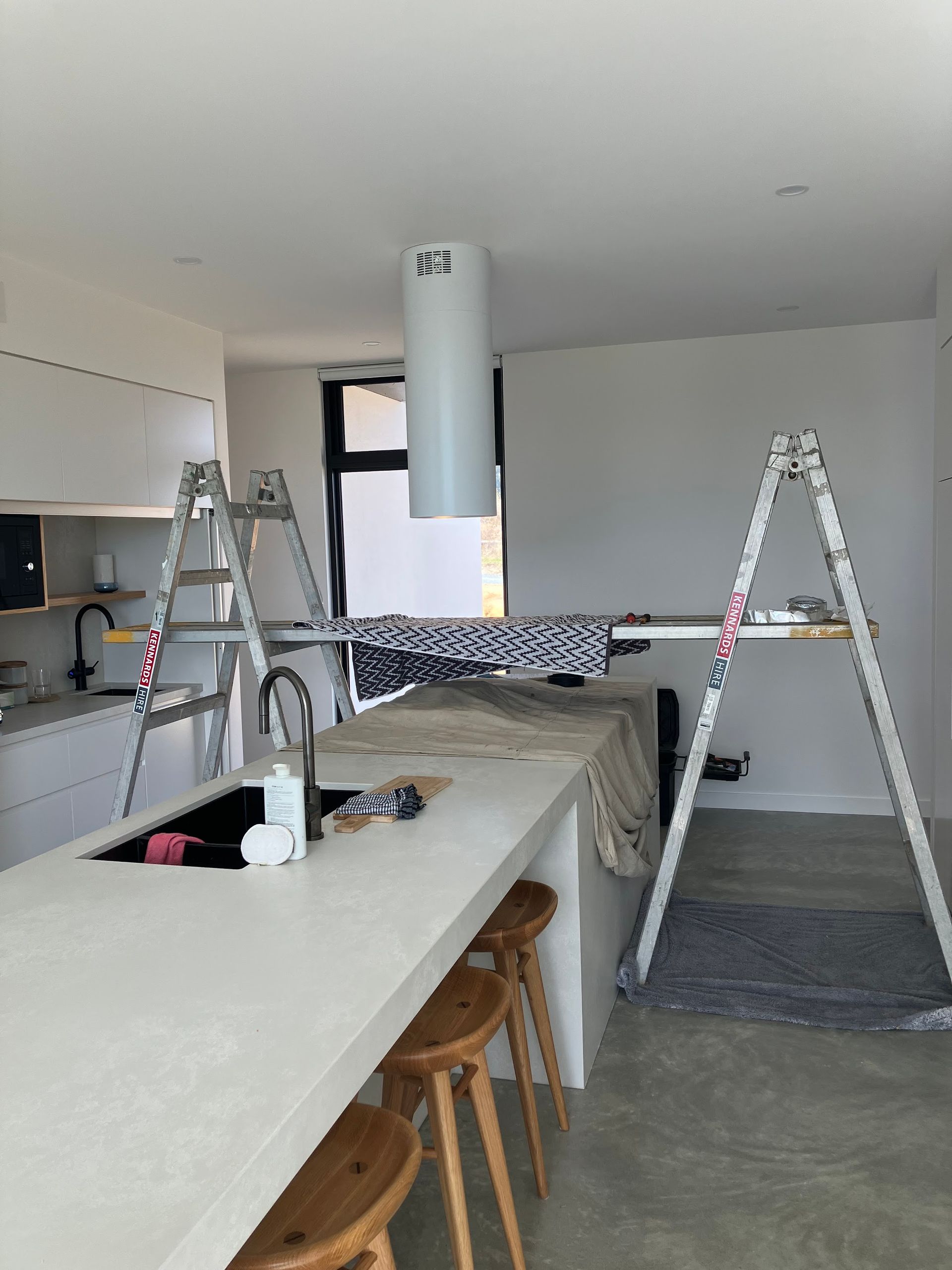 Kitchen under renovation with ladders, tools, and unfinished island in a bright open space — Plumbing in Canberra, ACT