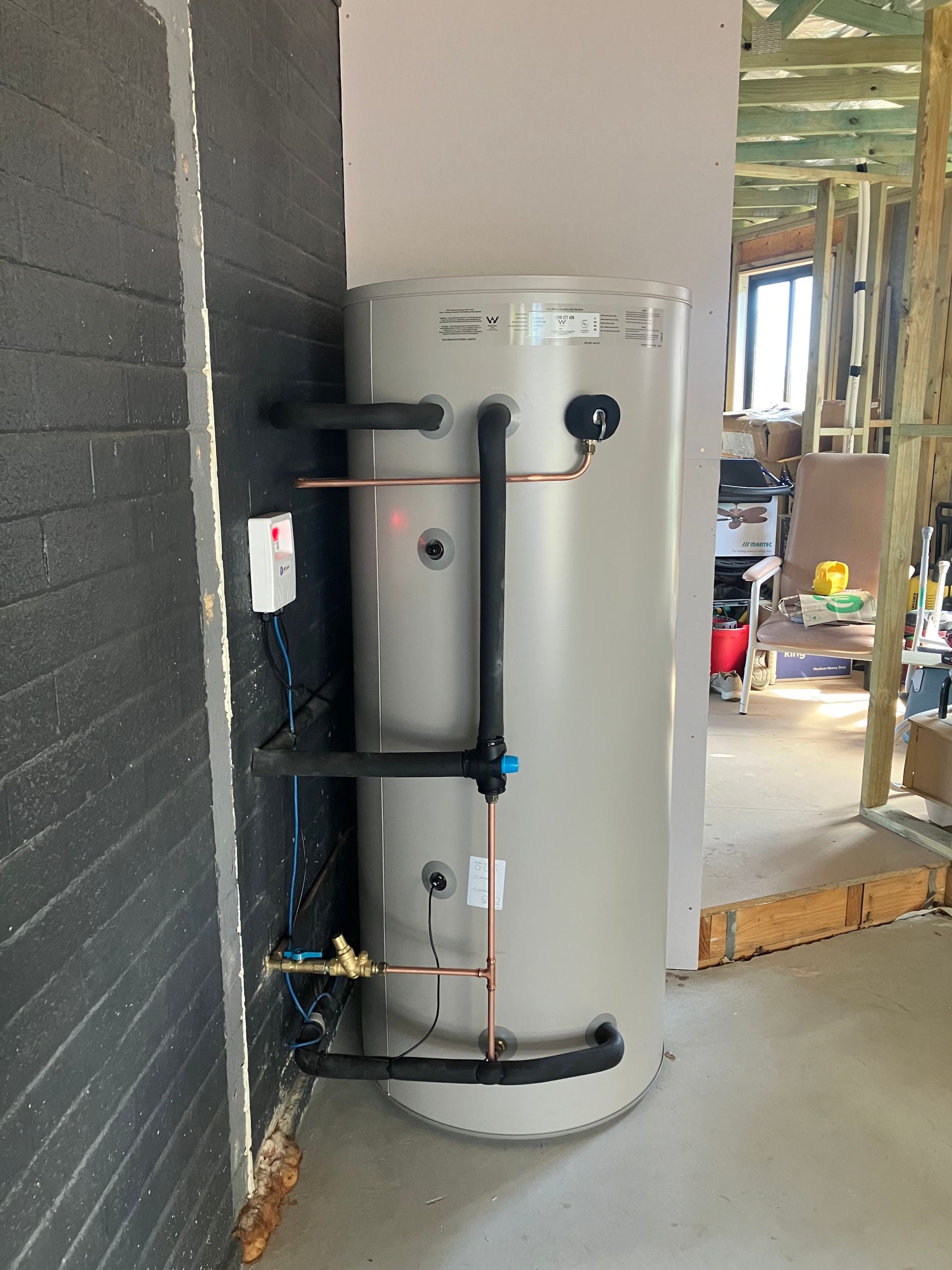 White water heater tank in an unfinished utility room with exposed framing and pipes — Plumbing in Canberra, ACT