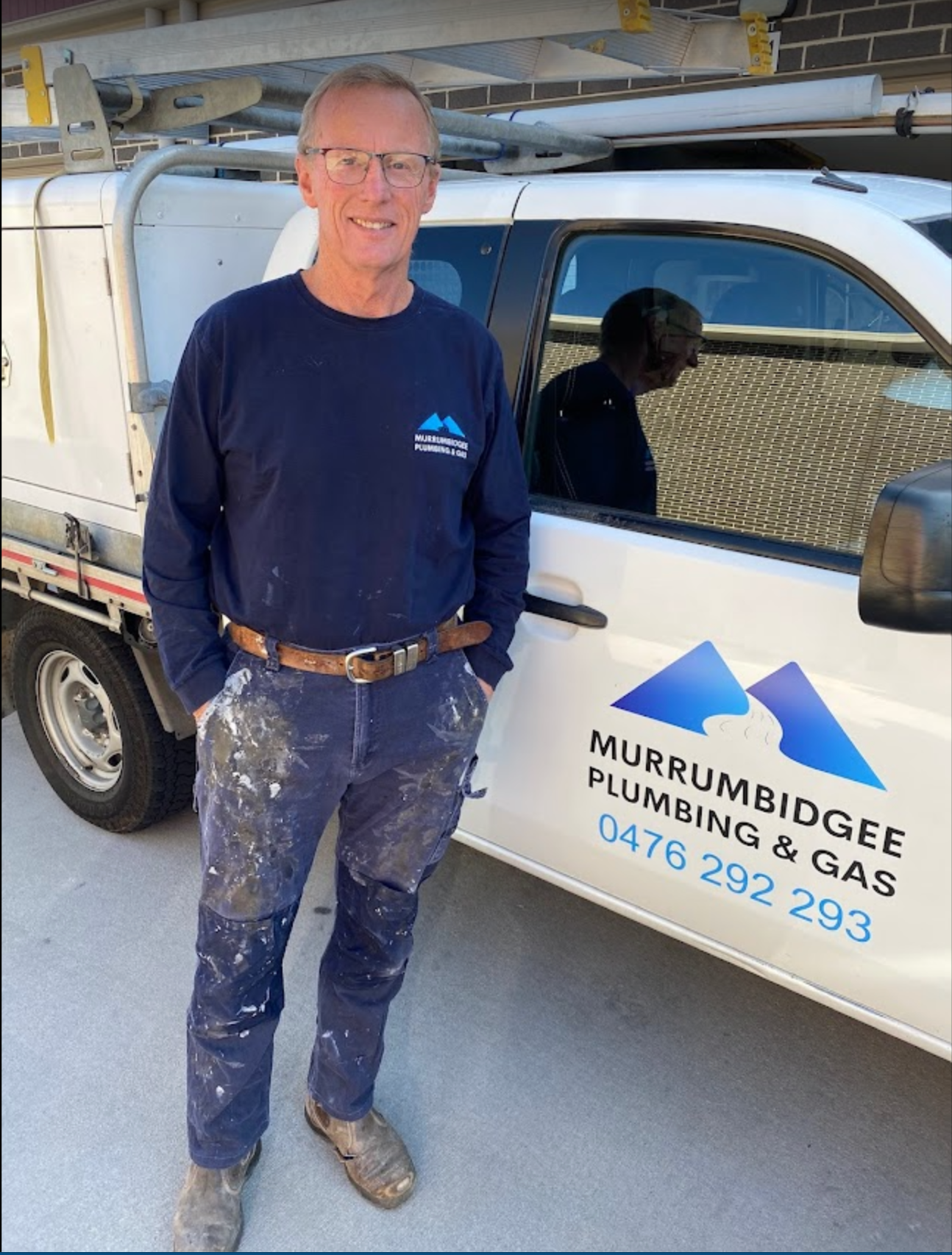 Plumber standing beside a white Murumbridge Plumbing & Gas service truck in a garage, holding a hose — Plumbing in Canberra, ACT