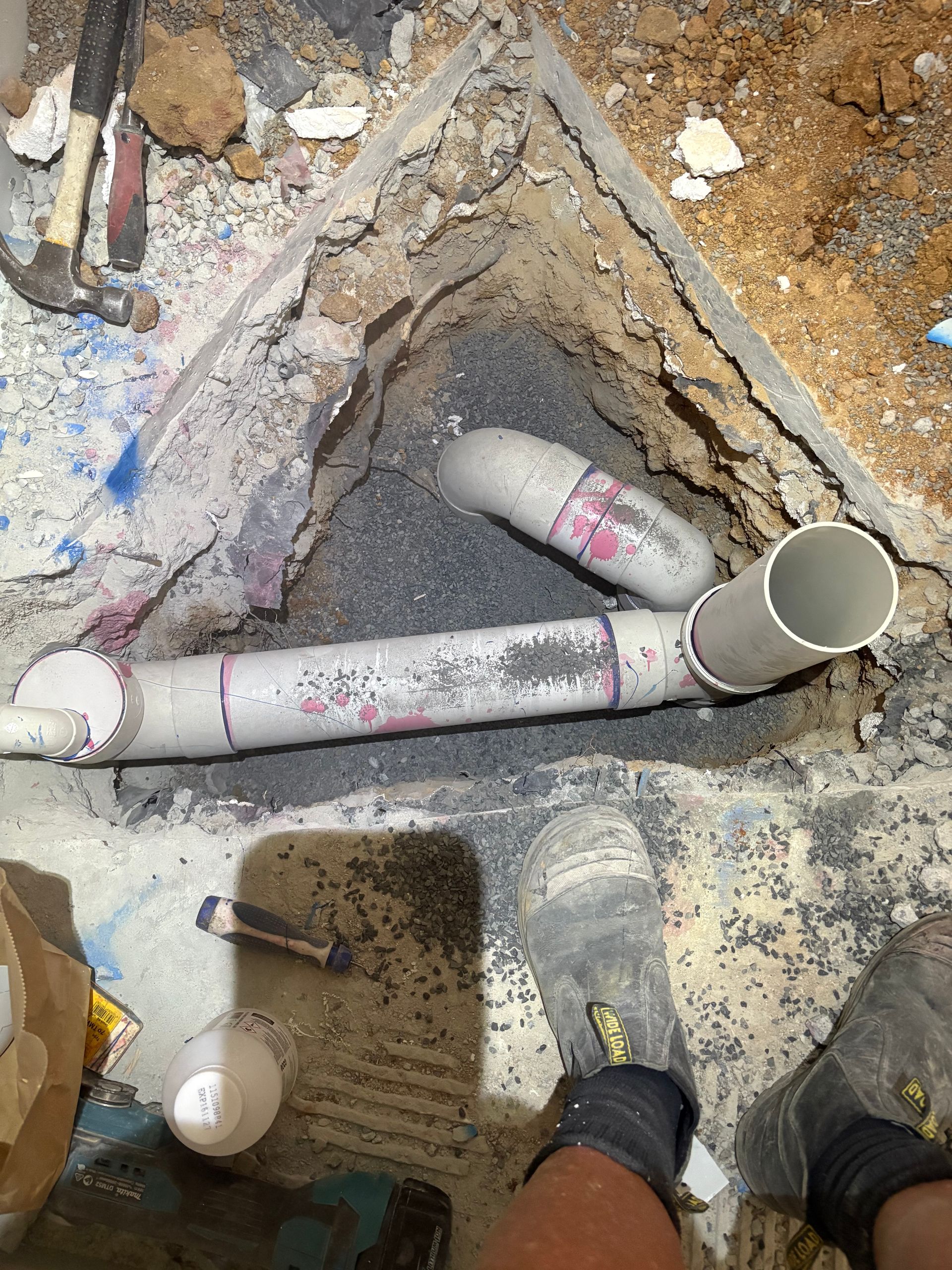 Worker’s feet beside exposed PVC pipes in a dirt trench under construction