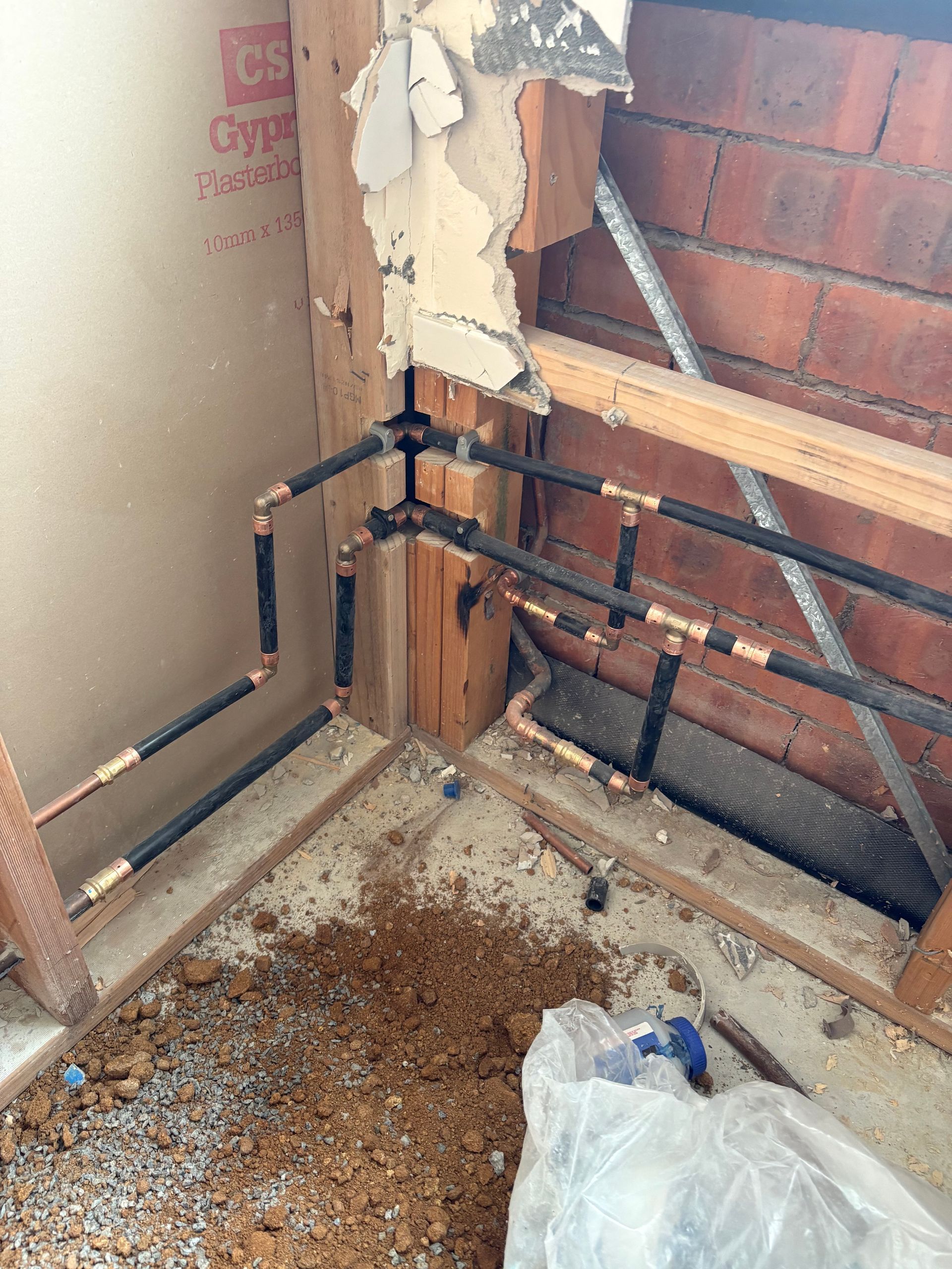 Damaged corner wall with exposed plumbing pipes, peeling drywall, and debris on the floor