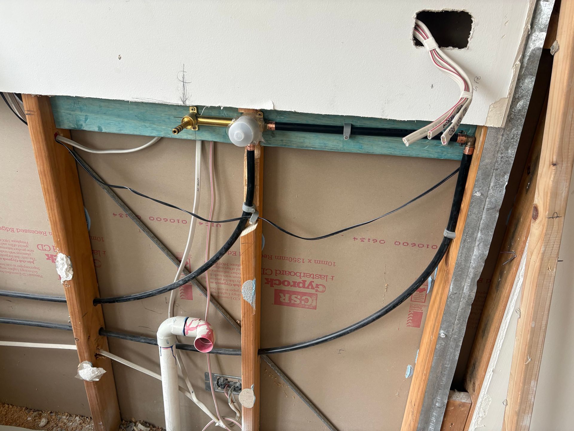 Exposed wall framing with visible pipes, wiring, and a cutout for electrical work.