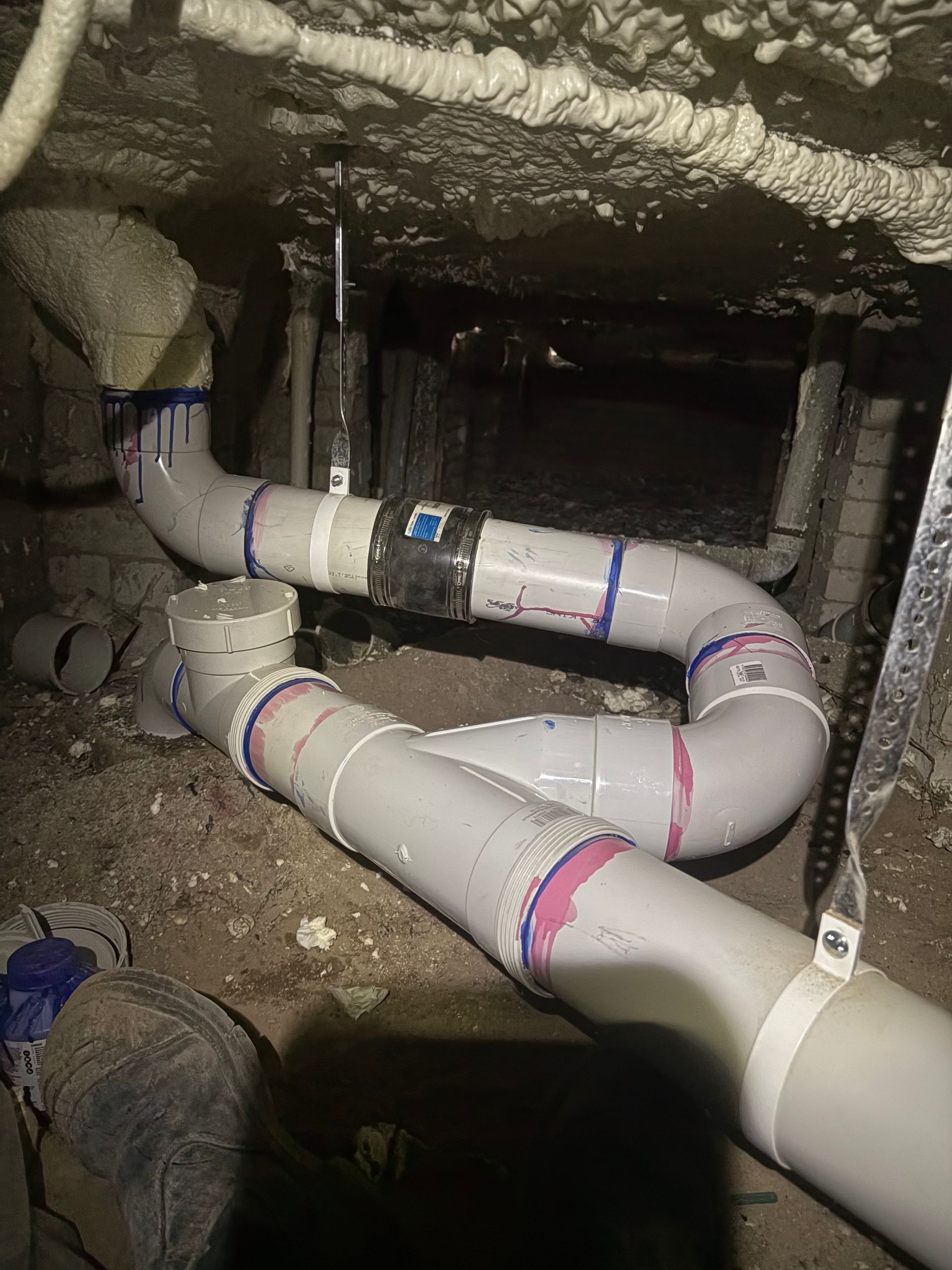 Insulated white pipes with purple bands running through a rough crawlspace under a building