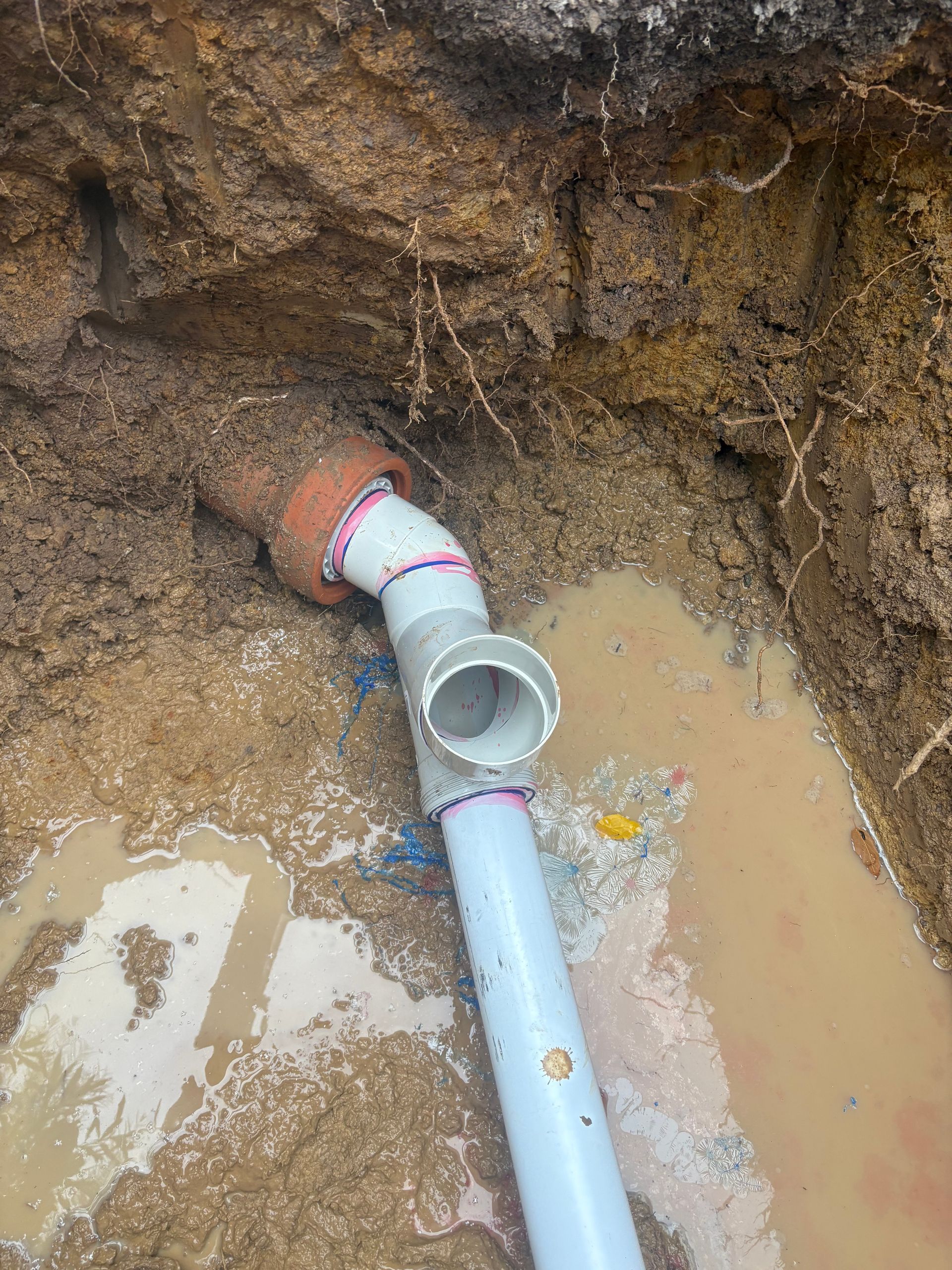 Broken blue pipe in muddy trench with standing water and exposed soil