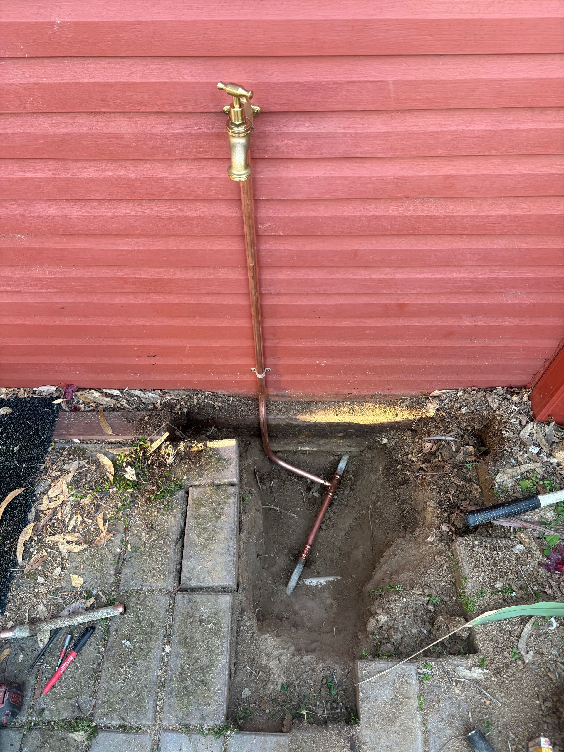Outdoor faucet and hose attached to a red wall above a wet concrete drain area