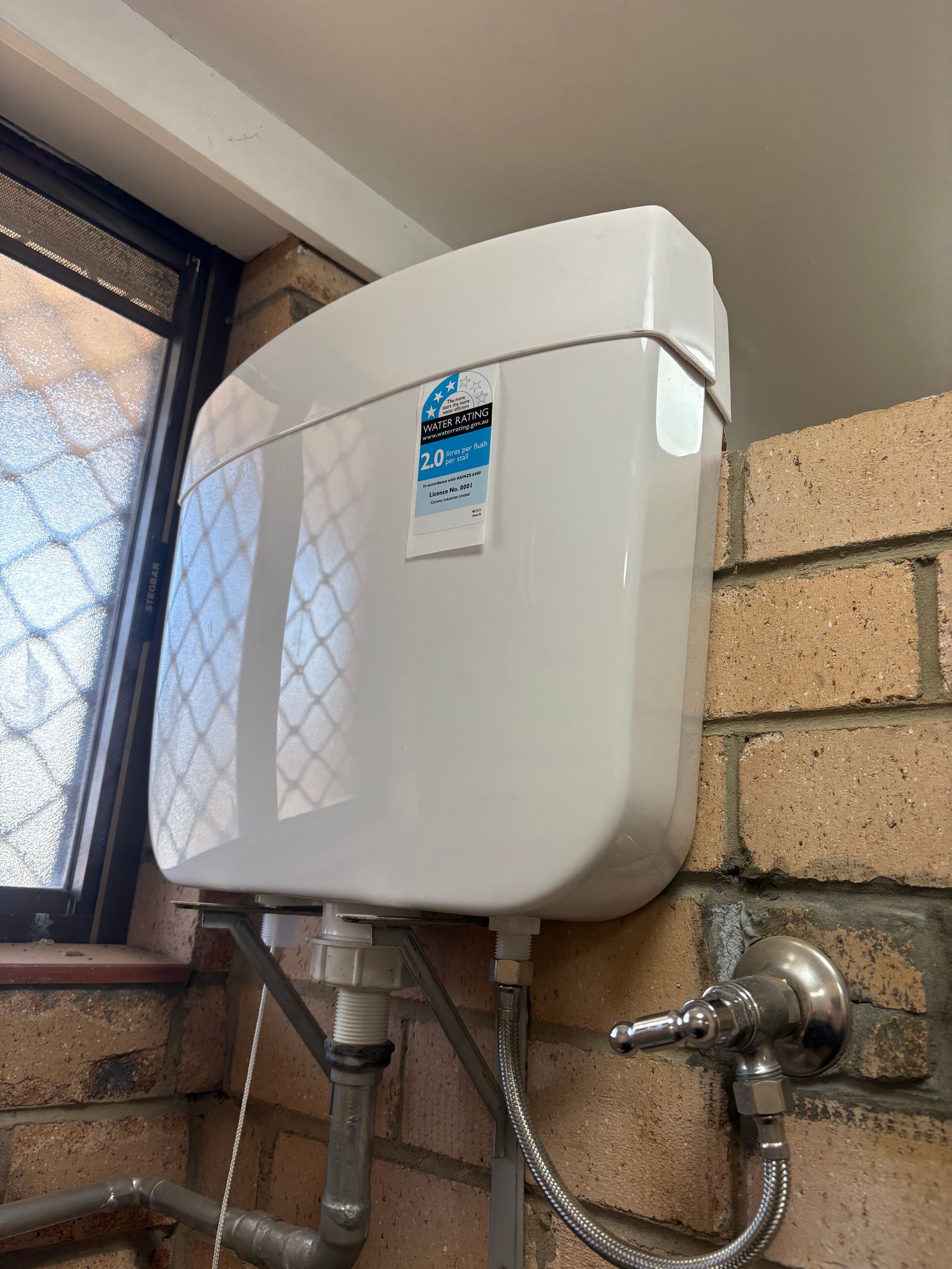 White wall-mounted water heater with pipes in a tiled utility room near a window