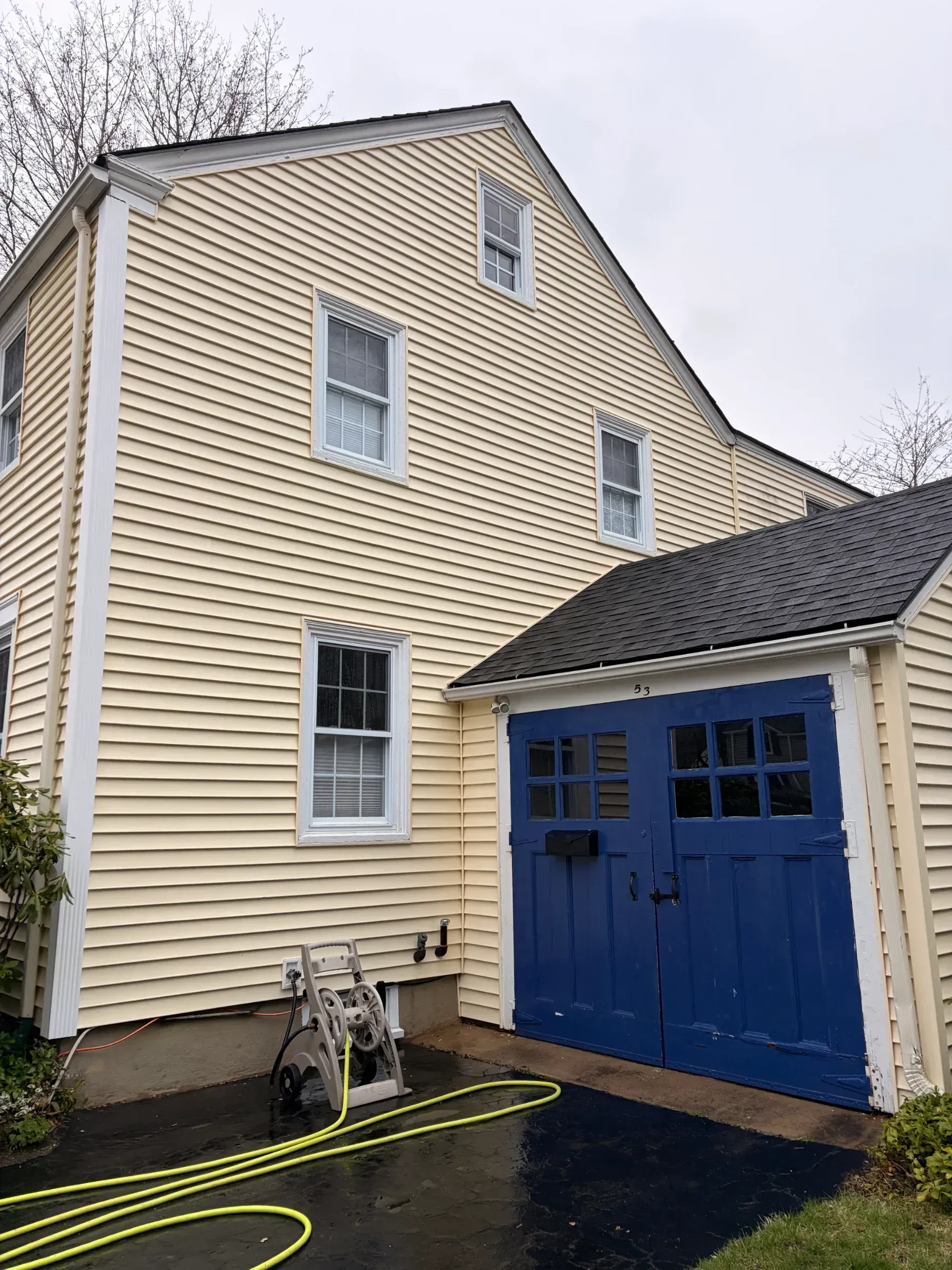Yellow house with blue garage doors and a bike parked outside on a wet driveway