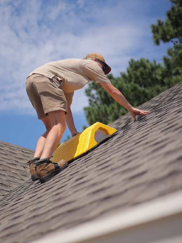 Worker on a sloped roof using a yellow tool under a blue sky