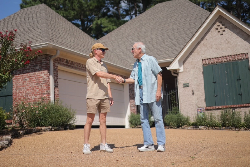 Two people shaking hands in front of a suburban house on a sunny day