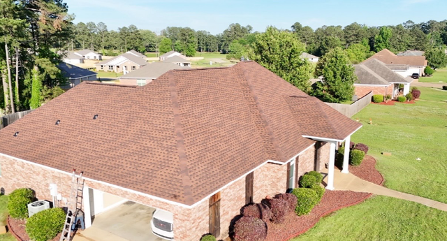 Aerial view of a brick house with a brown shingle roof and green lawn in a suburban neighborhood