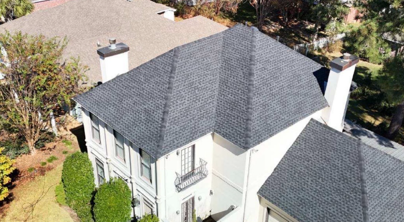 Aerial view of a white house with a dark gray roof and surrounding trees
