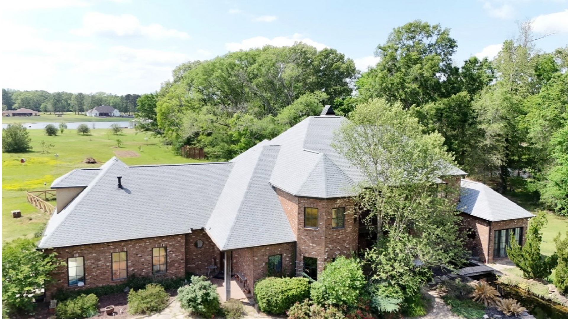 Aerial view of a brick house with a gray roof surrounded by lush green trees and lawn.