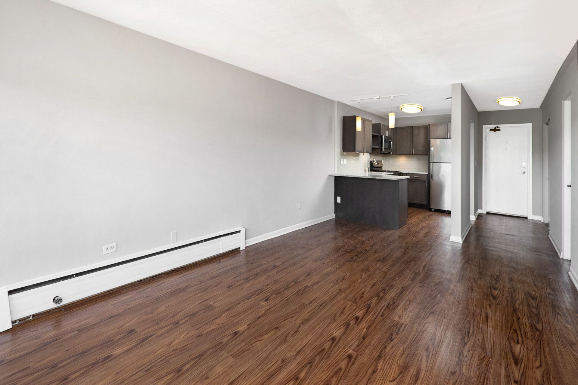an empty living room with wood flooring and a kitchen