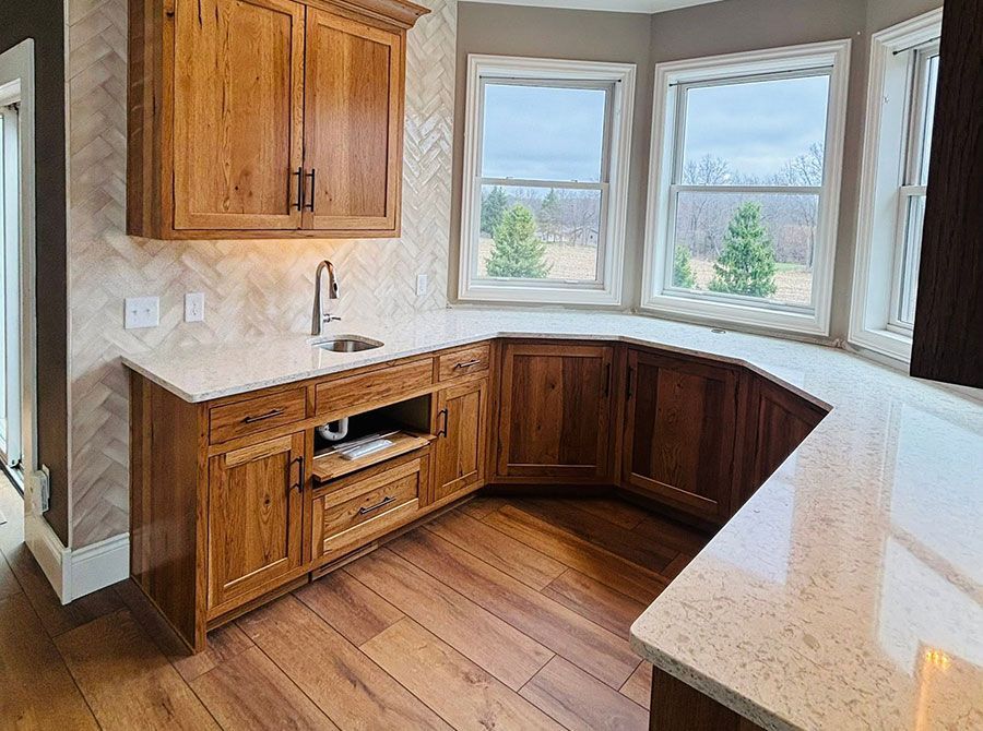 Empty kitchen corner with wood cabinets, white countertops, and bay windows over hardwood floors