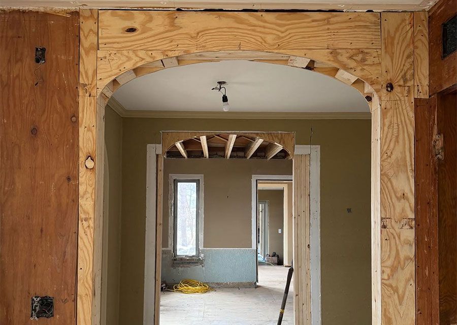 Partially renovated hallway with exposed wood framing, archway, and a room under construction beyond