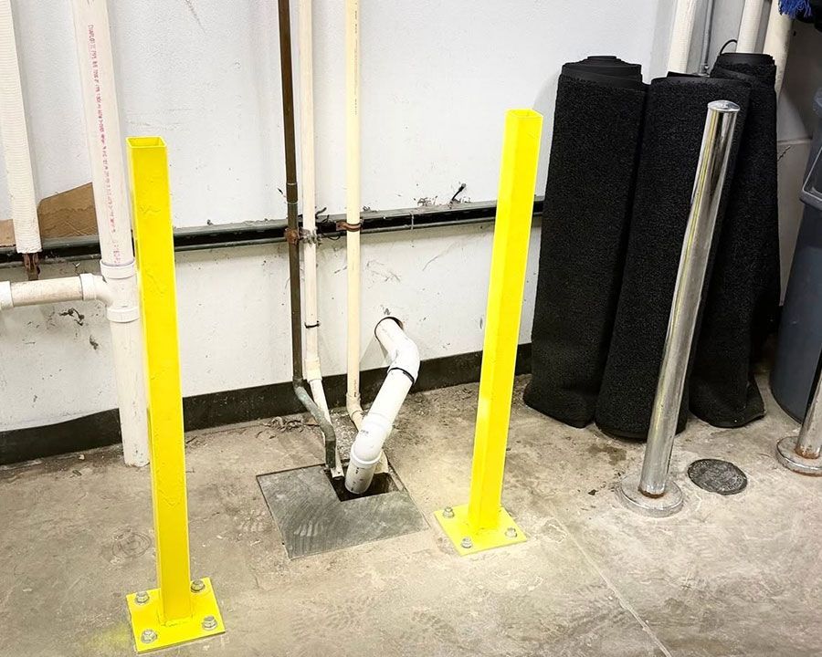 Yellow bollards around exposed white pipe in a utility area on a concrete floor