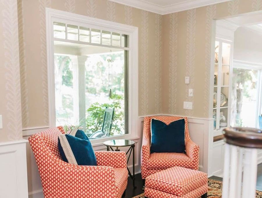 Bright living room with two coral patterned armchairs by large windows and a small side table.