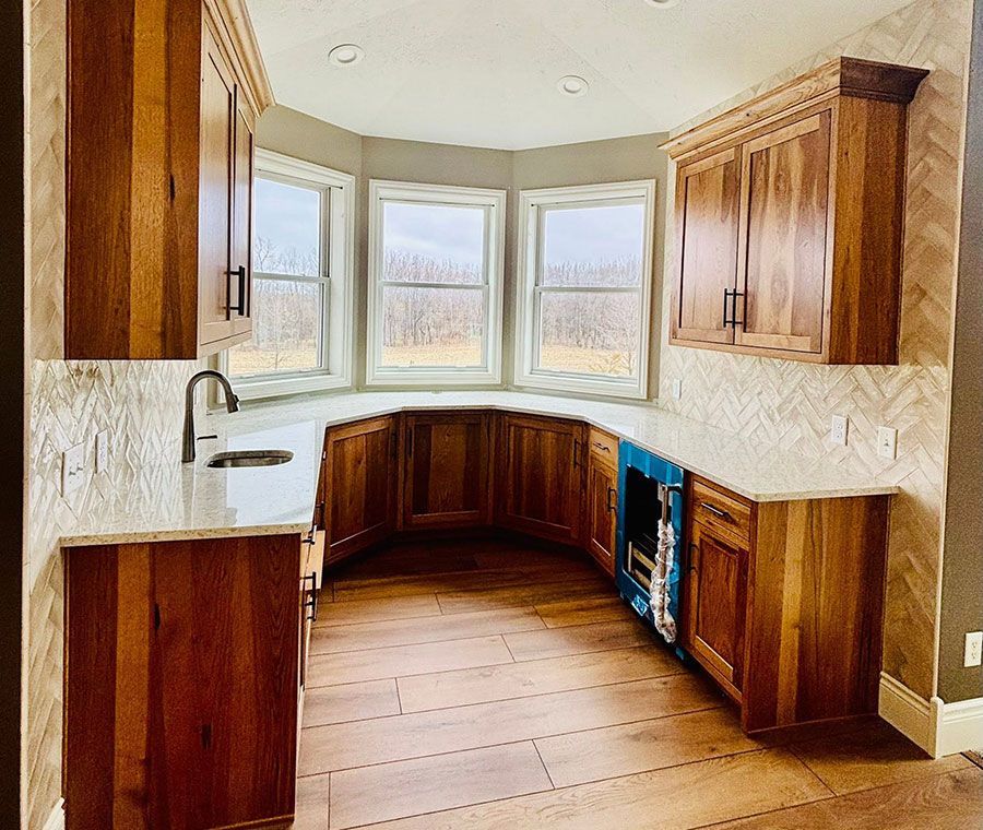 Bright kitchen with wood cabinets, white countertops, bay window, and unfinished floor near a blue appliance recess