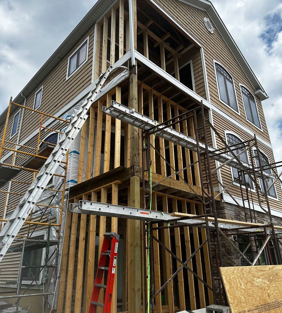 Two-story house under construction with exterior scaffolding, ladders, and exposed framing