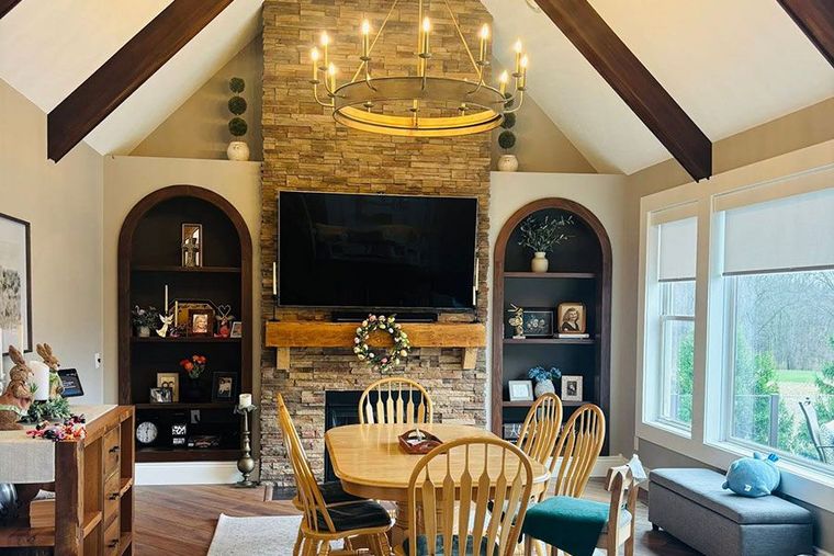 Cozy living room with vaulted ceiling, stone fireplace, wooden dining table, and large window views.