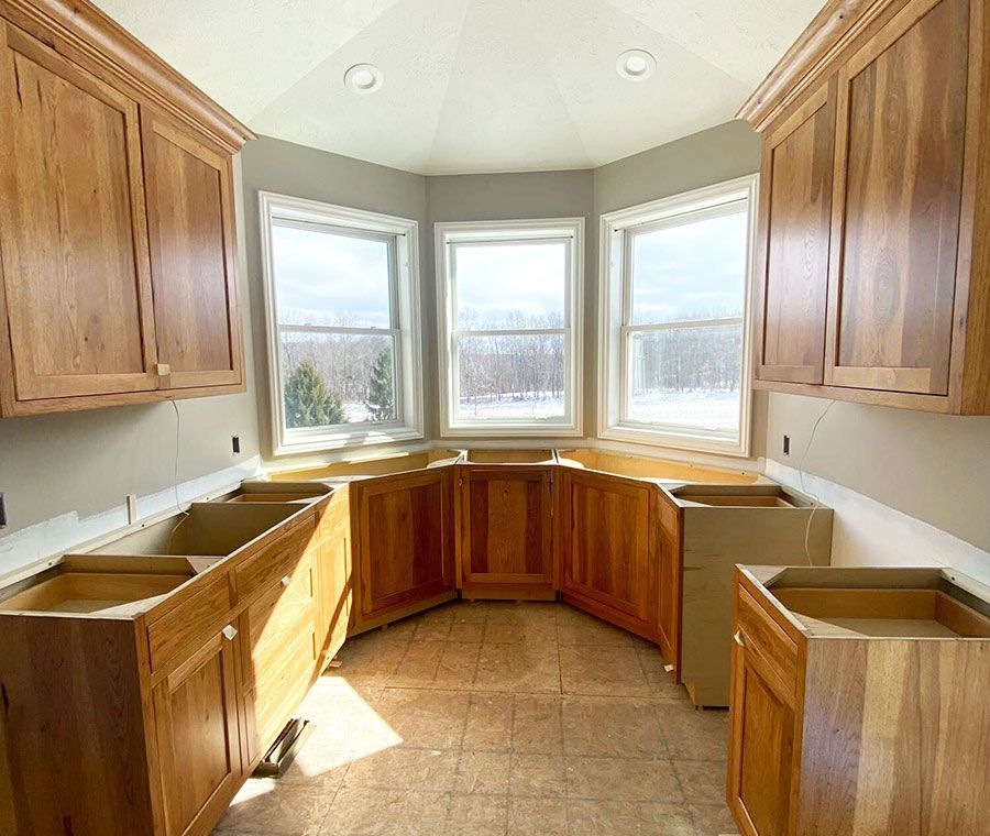 Bright kitchen with wood cabinets and unfinished countertops around a bay window.