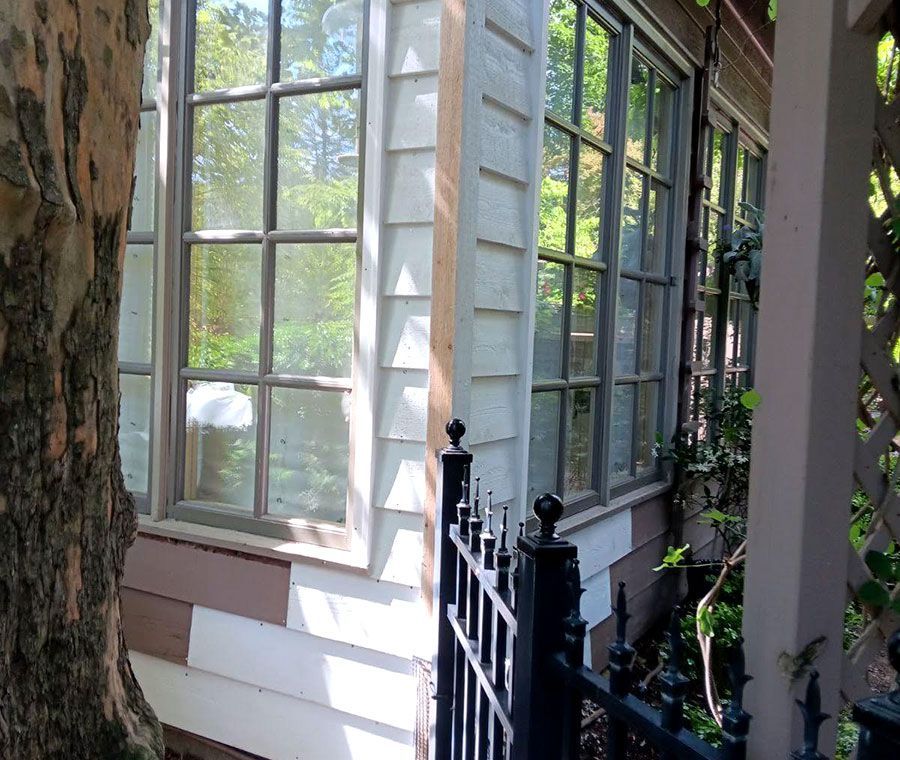White house windows beside a black iron fence, shaded by trees