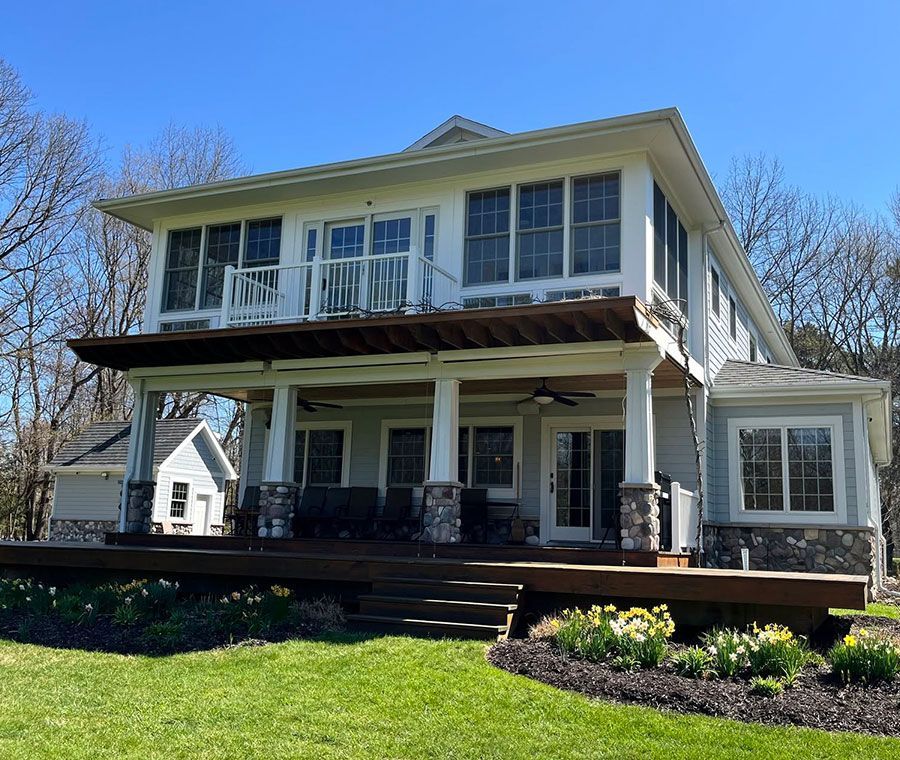 Two-story white house with porch, balcony, and green lawn in bright sunlight