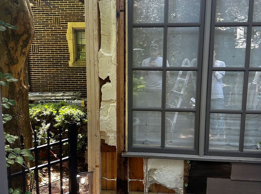Damaged window and crumbling wall beside a small balcony with plants outdoors