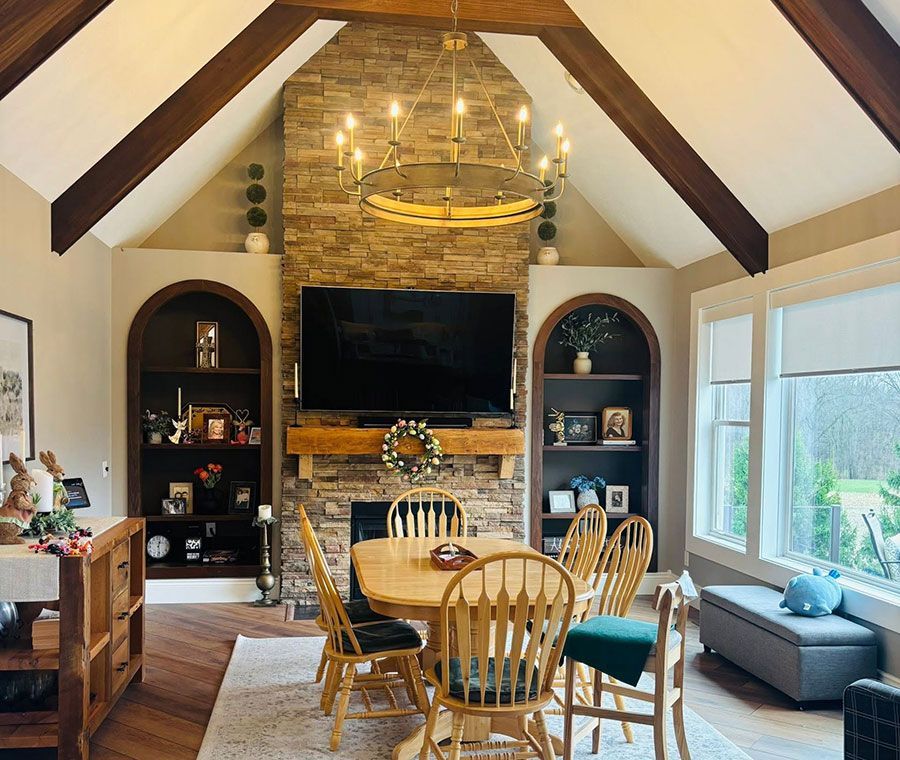 Cozy living room with stone fireplace, TV, dining table, built-in shelves, and large windows