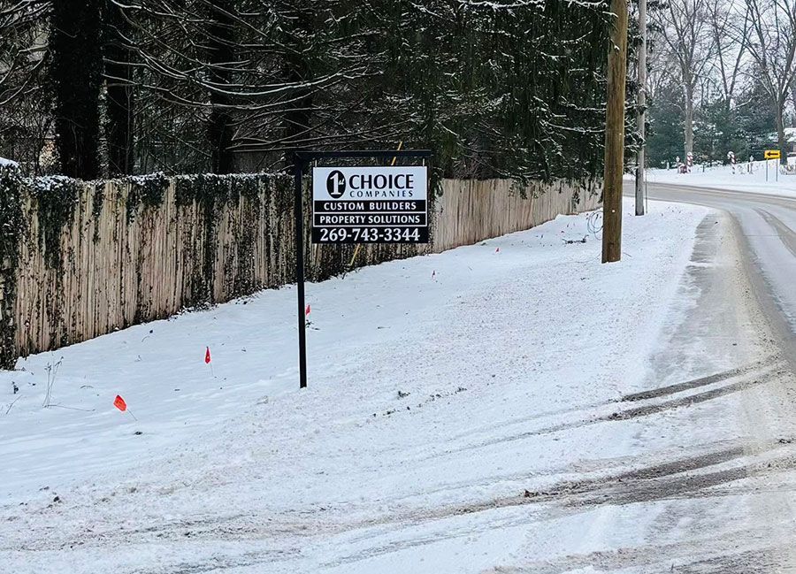 Snowy roadside with a real estate sign beside a snow-covered street and fence