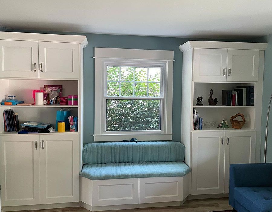Bright built-in cabinets flank a window seat with blue cushion in a cozy room.