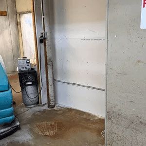 Wet concrete floor beside a wall and utility meter in a basement-like room