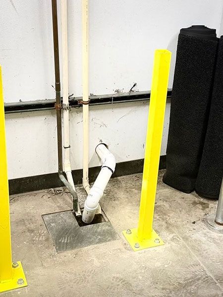 Basement utility area with exposed white pipe between bright yellow bollards and black protective posts