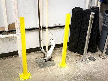 Bright yellow safety posts around pipes and floor drain in an industrial room