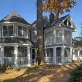 Gray Victorian-style house with white trim and wraparound porches beneath autumn trees